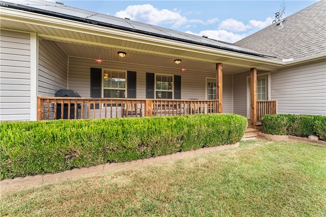 view of exterior entry with solar panels, a porch, and a lawn