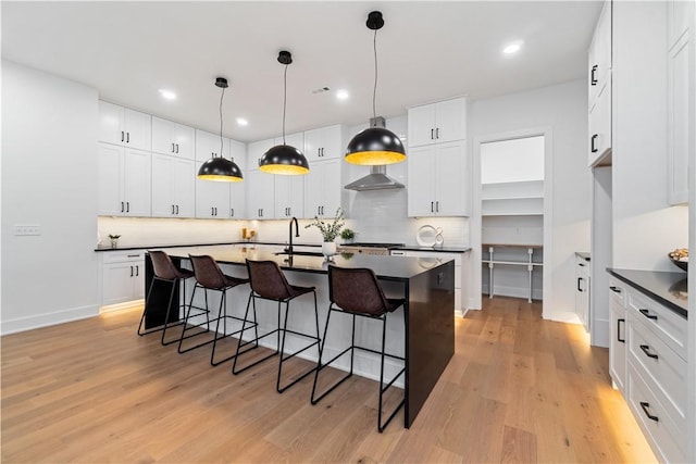 kitchen featuring dark countertops, decorative backsplash, a breakfast bar area, and wall chimney range hood