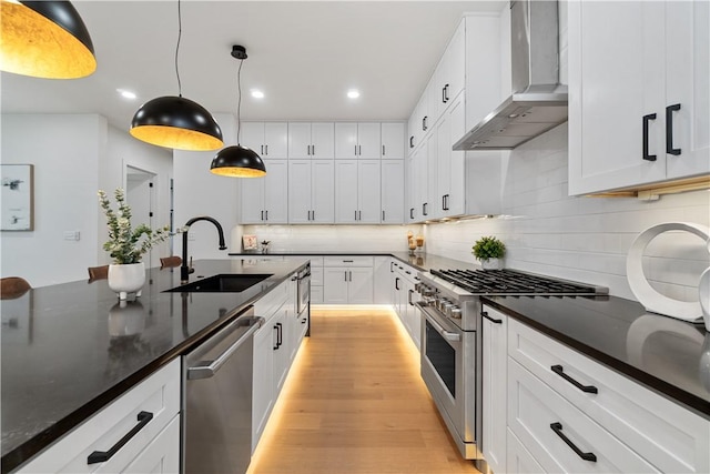 kitchen with a sink, recessed lighting, decorative backsplash, wall chimney range hood, and appliances with stainless steel finishes