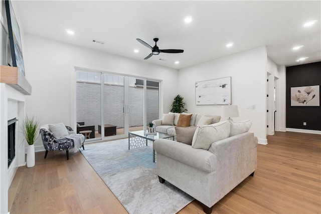 living area with a fireplace, light wood finished floors, visible vents, and a ceiling fan