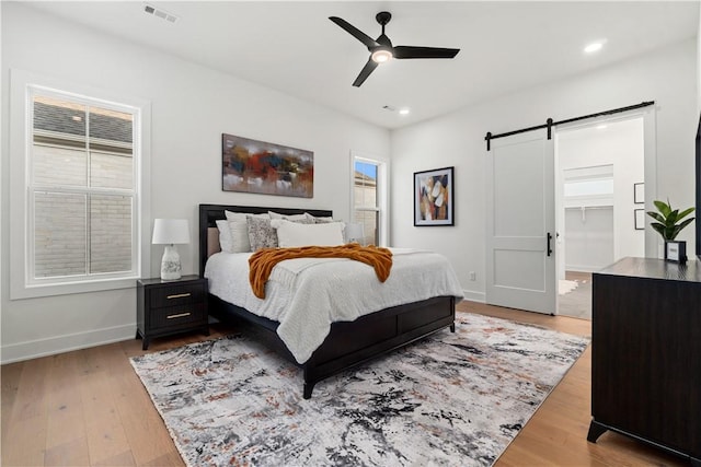 bedroom featuring a barn door, wood finished floors, visible vents, and baseboards