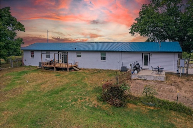 back house at dusk featuring central air condition unit, a deck, and a lawn