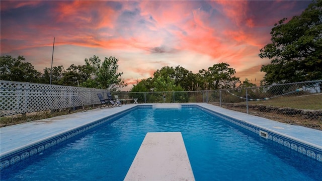 pool at dusk featuring a diving board