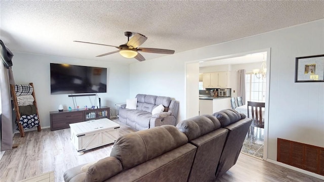 living room with a textured ceiling, ceiling fan with notable chandelier, and light hardwood / wood-style flooring