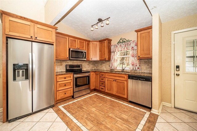 kitchen with lofted ceiling, sink, light tile patterned floors, a textured ceiling, and appliances with stainless steel finishes