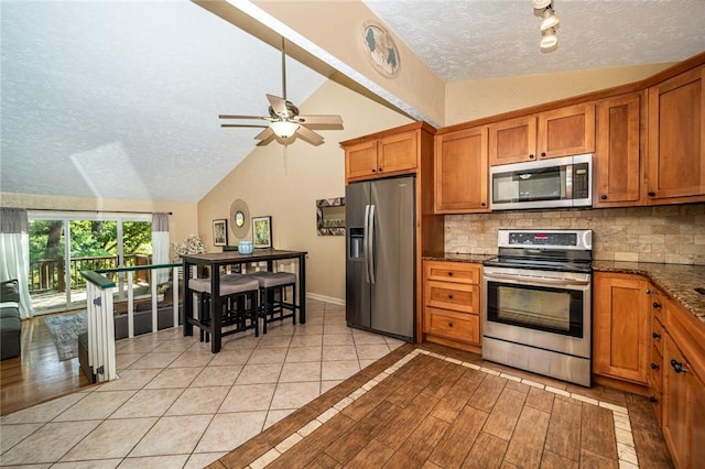 kitchen featuring vaulted ceiling, dark stone counters, stainless steel appliances, and backsplash