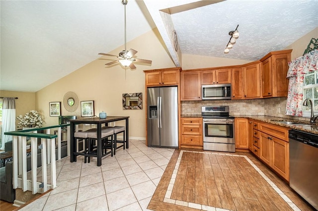 kitchen with stainless steel appliances, decorative backsplash, vaulted ceiling, a sink, and dark stone counters