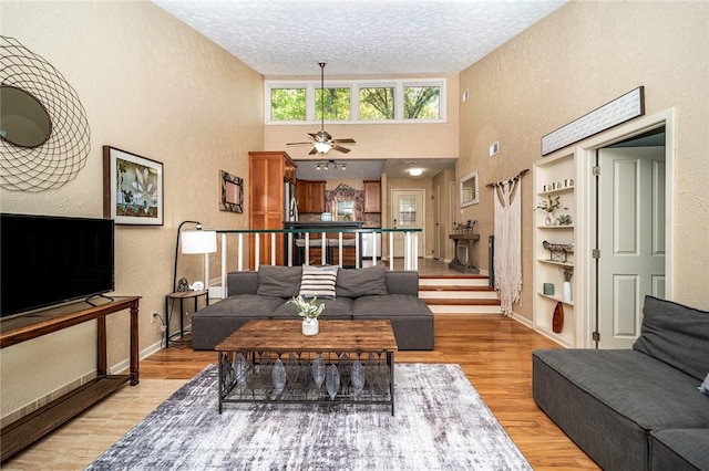 living area featuring a textured wall, light wood-style floors, ceiling fan, a textured ceiling, and baseboards