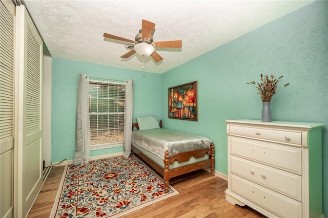 bedroom with light wood finished floors, ceiling fan, baseboards, and a textured ceiling