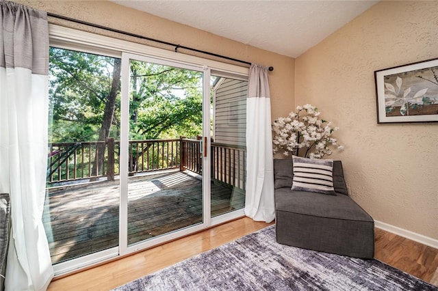 doorway to outside featuring vaulted ceiling, a textured wall, wood finished floors, and baseboards