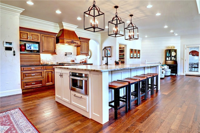 kitchen featuring pendant lighting, a breakfast bar, dark hardwood / wood-style floors, a kitchen island with sink, and stainless steel oven