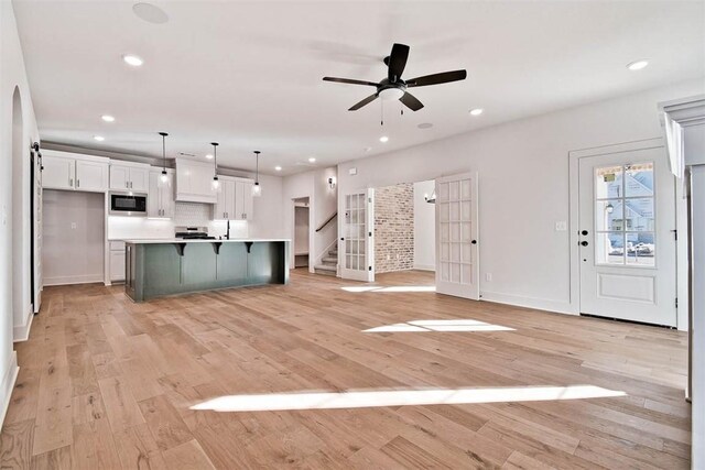 interior space with built in microwave, white cabinetry, decorative light fixtures, light wood-type flooring, and a large island