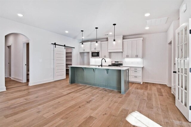 kitchen featuring white cabinetry, pendant lighting, a barn door, and an island with sink