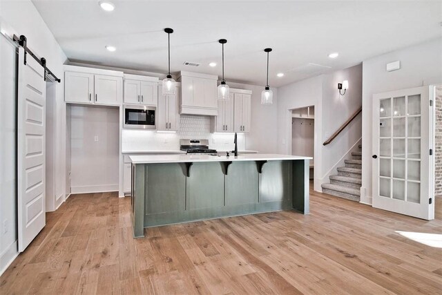 kitchen with white cabinets, built in microwave, decorative light fixtures, a barn door, and a large island with sink