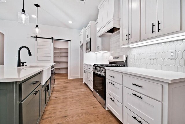 kitchen featuring white cabinetry, hanging light fixtures, a center island with sink, appliances with stainless steel finishes, and custom range hood