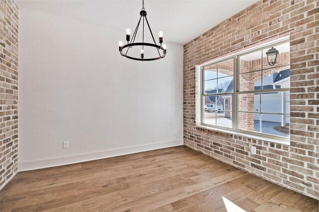 empty room with an inviting chandelier, wood-type flooring, and brick wall