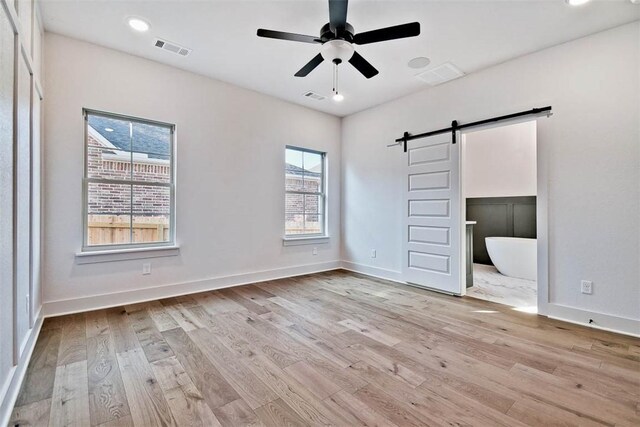 unfurnished bedroom featuring a barn door, light hardwood / wood-style floors, and ensuite bath