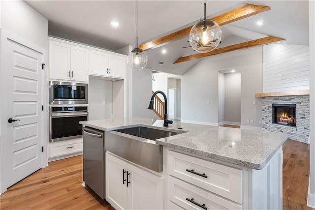 kitchen featuring stainless steel appliances, white cabinets, vaulted ceiling with beams, a stone fireplace, and hanging light fixtures