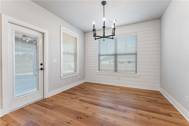 unfurnished dining area with wood walls, wood-type flooring, and an inviting chandelier