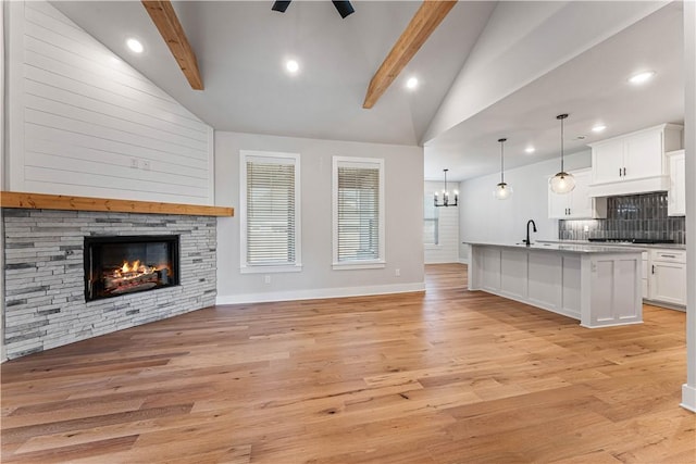 unfurnished living room featuring lofted ceiling with beams, ceiling fan, a stone fireplace, and light hardwood / wood-style flooring