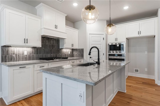 kitchen with sink, stainless steel appliances, pendant lighting, a center island with sink, and white cabinets