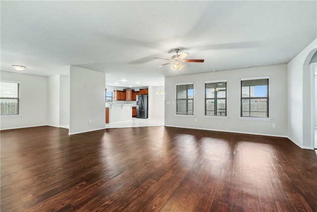 unfurnished living room featuring ceiling fan, dark wood-type flooring, and a textured ceiling