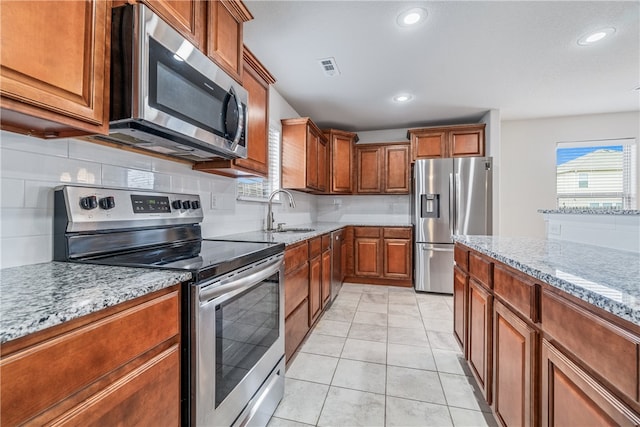 kitchen with appliances with stainless steel finishes, light stone countertops, sink, and light tile patterned floors