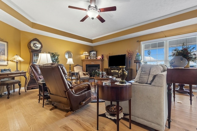 living room featuring ceiling fan, light hardwood / wood-style flooring, a raised ceiling, and ornamental molding