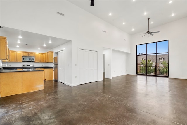 kitchen featuring a high ceiling, appliances with stainless steel finishes, open floor plan, concrete floors, and baseboards