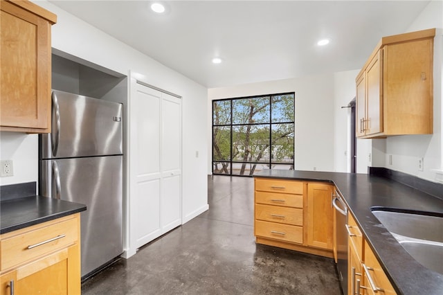 kitchen with appliances with stainless steel finishes, dark countertops, built in desk, and finished concrete flooring