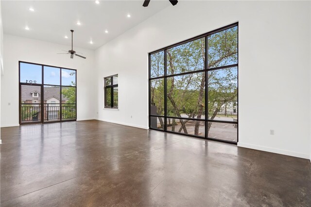 spare room with ceiling fan, concrete floors, a towering ceiling, and baseboards