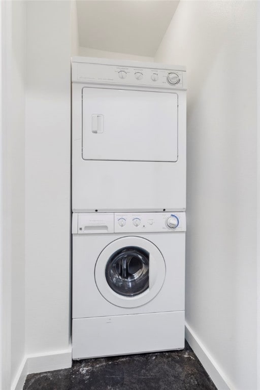 clothes washing area featuring stacked washing maching and dryer and baseboards