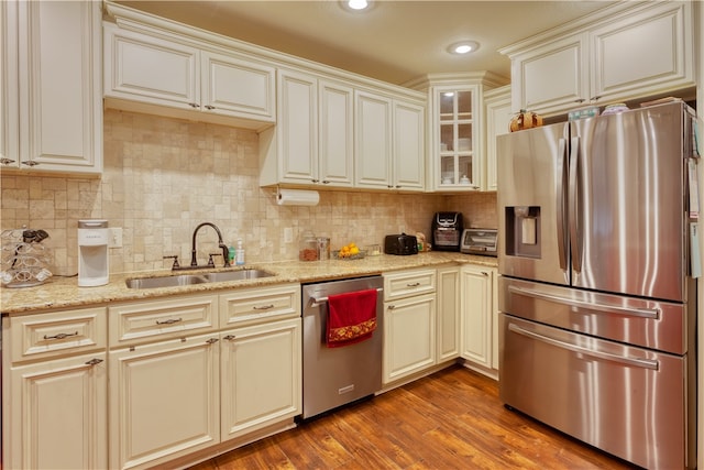 kitchen with sink, cream cabinets, backsplash, hardwood / wood-style flooring, and appliances with stainless steel finishes