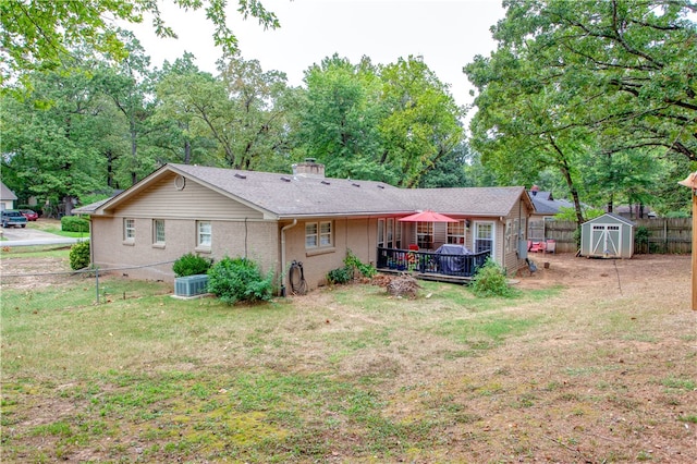 rear view of property with cooling unit, a deck, a lawn, and a shed