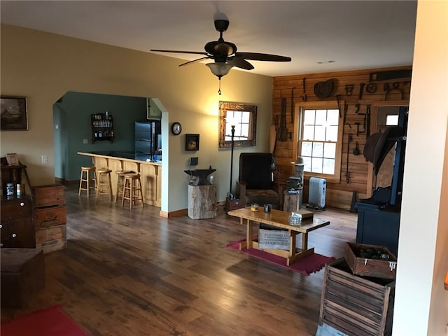 living room with wood walls, ceiling fan, bar area, and dark hardwood / wood-style flooring