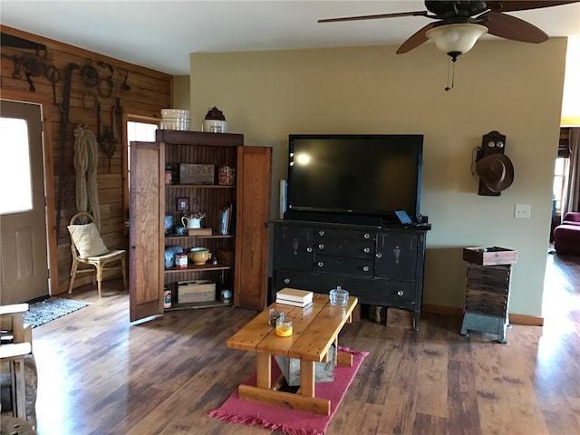 living room with wood walls, ceiling fan, and dark wood-type flooring