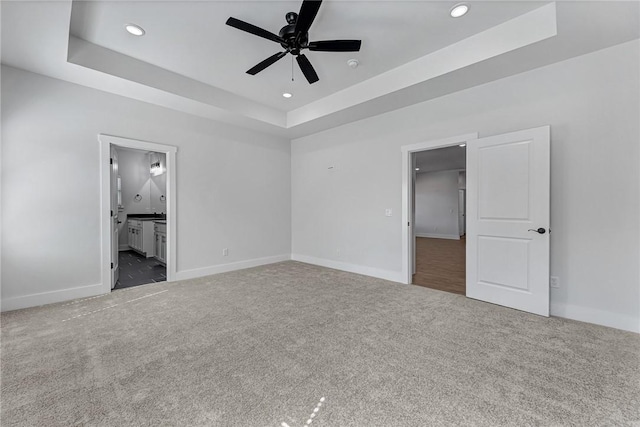 unfurnished bedroom featuring carpet, a tray ceiling, and baseboards