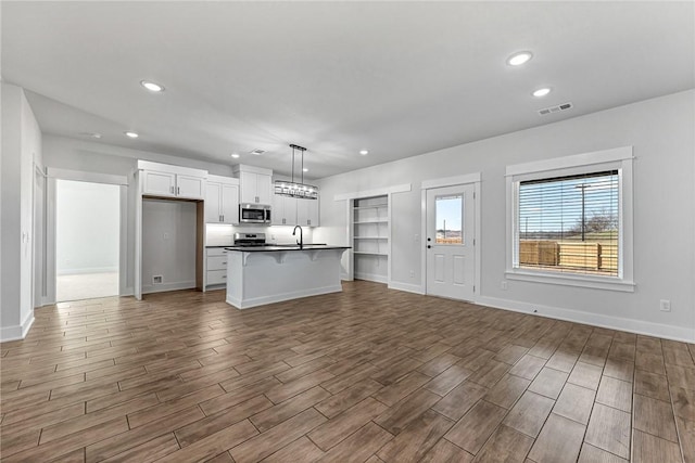 kitchen with a sink, visible vents, open floor plan, appliances with stainless steel finishes, and dark countertops