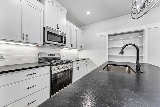 kitchen featuring backsplash, appliances with stainless steel finishes, white cabinetry, a sink, and dark stone countertops