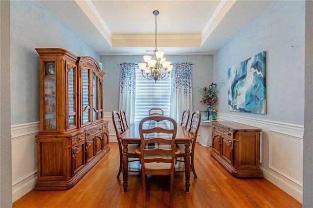 dining room with crown molding, light hardwood / wood-style flooring, a tray ceiling, and a notable chandelier