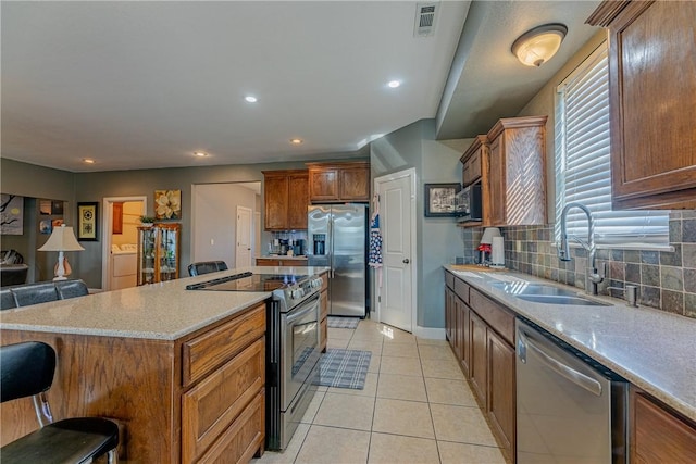 kitchen with light tile patterned floors, a kitchen bar, stainless steel appliances, sink, and a center island