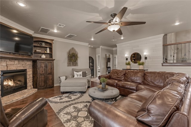 living room featuring ceiling fan, a stone fireplace, crown molding, and dark hardwood / wood-style flooring