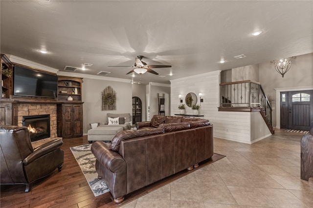 living room with light hardwood / wood-style floors, ceiling fan with notable chandelier, a stone fireplace, and ornamental molding