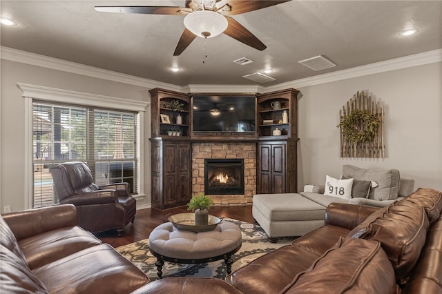 living room featuring a stone fireplace, ornamental molding, dark wood-type flooring, and ceiling fan