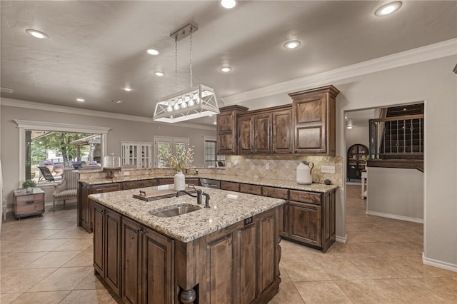 kitchen featuring pendant lighting, decorative backsplash, a center island with sink, and sink