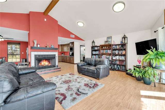 living room featuring ceiling fan, beam ceiling, hardwood / wood-style floors, and a tile fireplace