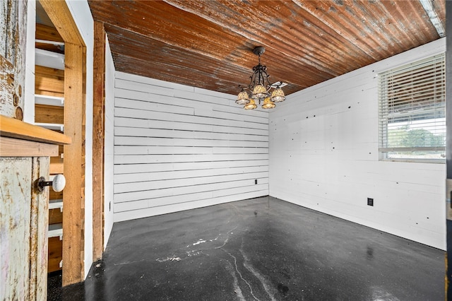 unfurnished dining area featuring a notable chandelier, wooden walls, and wood ceiling