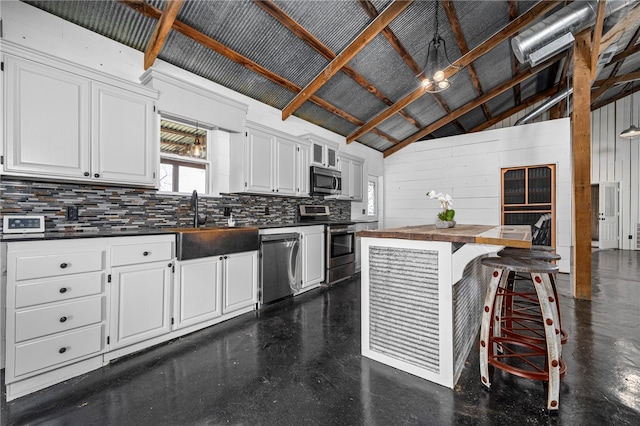 kitchen featuring appliances with stainless steel finishes, decorative backsplash, a kitchen breakfast bar, white cabinetry, and wooden walls