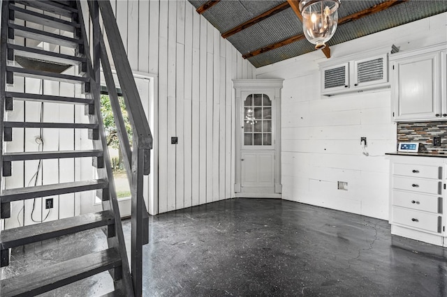 staircase with wooden walls, vaulted ceiling, and concrete flooring