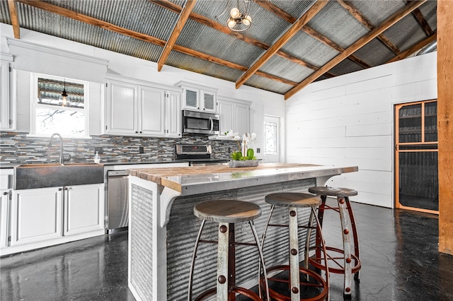 kitchen featuring a center island, vaulted ceiling, white cabinetry, appliances with stainless steel finishes, and wooden counters